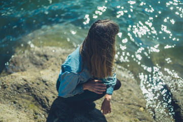 Young woman relaxing on rock by the water