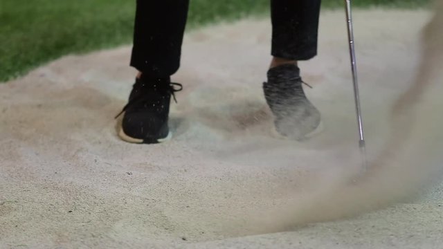 Slow motion shot of golfer swinging golf ball on sand indoor at golf club. Sport and recreation concept.