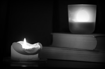 Burning candle and old books in the dark close up. Black and white