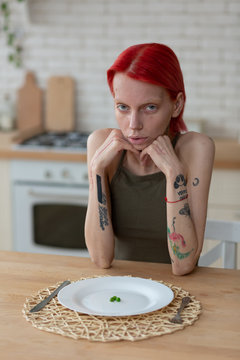 Woman with anorexia sitting in the kitchen with empty plate