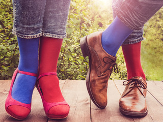 Men's and women's legs in fashionable shoes, bright, multi-colored socks on a wooden terrace on the...