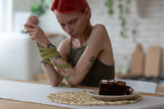 Red-haired anorexic woman looking at plate with dessert