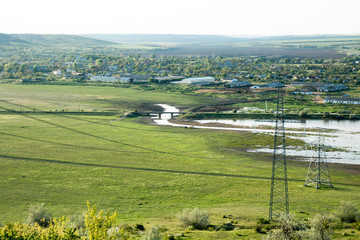 rural village in the green valley with river and high voltage electric poles across the valley