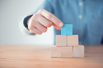 Hand putting blank blue wood cube block on top pyramid, for create icon symbol to success concept.
