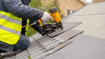 Deurstickers Workman using pneumatic nail gun install tile on roof of new house under construction © brizmaker