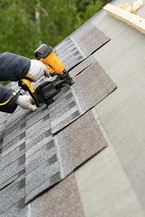 Workman using pneumatic nail gun install tile on roof of new house under construction