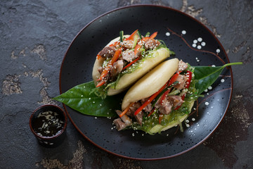 Chinese steamed baozi with chicken and vegetables on a plate, horizontal shot over brown stone...