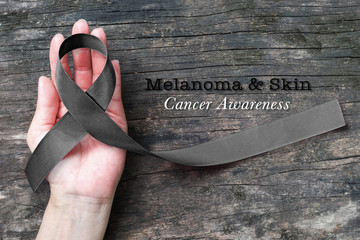 Melanoma and skin cancer black awareness ribbon on human helping hand old aged background