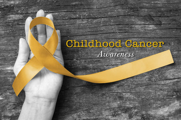 Childhood cancer awareness with gold ribbon symbolic color on helping hand on old aged wood