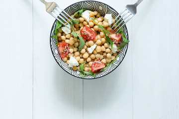 A bowl of healthy vegetarian salad with chickpeas, two forks on white wooden background, top view,copy space.