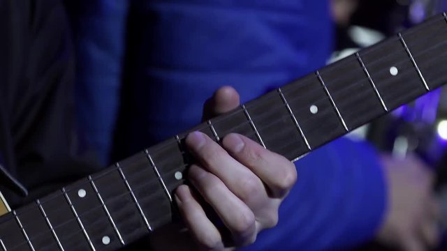 Male musician wearing black outfit professionally plays cute acoustic guitar standing on stage during some concert event.