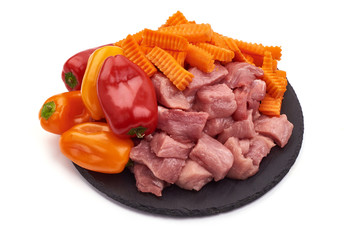 Raw pork pieces with vegetables on a slate shale plate, close-up, isolated on white background