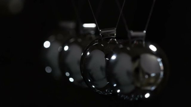 Slow Hit Newtons Balls. Loop. Steel shiny balls suspended on a dark background. They interact with each other, transferring the force of impact. Filmed at a speed of 240fps