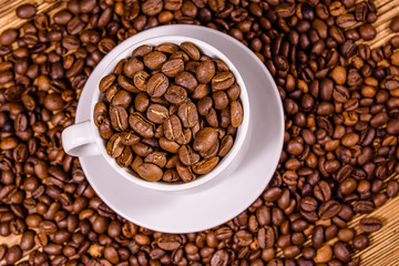 White cup filled with coffee beans on wooden table. Top view