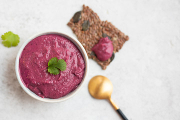 Top view of beet or beetroot hummus served with cilantro and seed crackers and a golden spoon on a natural stone light background. Copy space. 