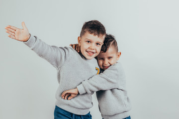 Photo of two adorable boys brothers or friends embracing and smiling joyfully on a gray background.