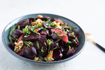 Roasted beet/beetroot, apples, walnuts, microgreens, winter salad, scallions salad in a blue pottery bowl with homemade vinaigrette and golden spoon on light background. 