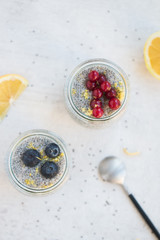 Top view of jars of chia seed pudding made with chia seeds and almond milk and berries, gooseberries, blueberries, lemon zests,  shallow depth of field, copy space and light background. 