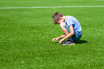 Fototapeta na wymiar Sad alone kid sitting on the football field