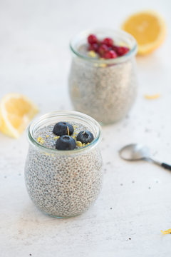 Jars of chia seed pudding made with chia seeds and almond milk and berries, goose berries, blueberries, lemon zests,  shallow depth of field, copy space and light background. 