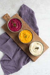 Three hummus dips, beet hummus, sweet potato or carrot or pumpkin hummus and parsnip hummus on a...