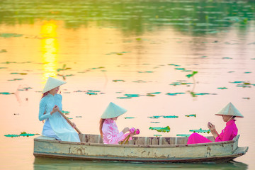 Vietnamese female group on a lotus wooden boat Asian women sit on a wooden boat to collect lotus flowers. Three beautiful women wearing a Vietnamese dress with pink lotus flowers.