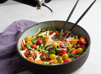 Fennel, flat green beans, cherry tomatoes, radish, carrot, cilantro, parsley, basil, hemp seeds, olive oil, balsamic vinegar salad in pottery dish with olive oil drops. Side view