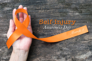 Self- injury awareness day, March 1, Orange ribbon on human hand old aged background.