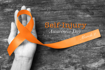 Self- injury awareness day SIAD, March 1with Orange ribbon on human hand old aged background.