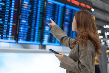 woman using smartphone with flight information board at airport