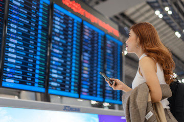 woman using smartphone with flight information board at airport