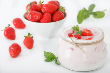 Healthy strawberry yoghurt in a glass jar with scattered berries over white background