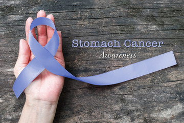 Periwinkle ribbon with Stomach cancer awareness on woman human hand on aged grunge wood background: