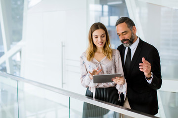 Handsome smiling mature businessman and his cute young female coworker with digital tablet in the...