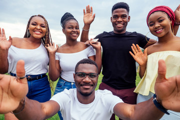 group of five friends female and male taking selfie on camera smartphone and having fun outdoors...