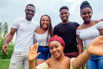 group of five friends female and male taking selfie on camera smartphone and having fun outdoors...