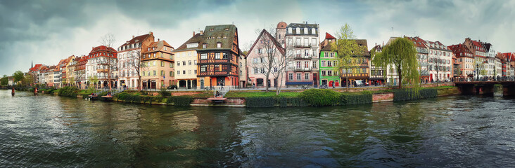 Spring panorama of Strasbourg city in front of Quai des Bateliers street along water canal. Fachwerk timber framing colorful houses. Traditional architecture near the river bank.