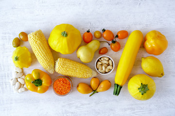 Assorted types of yellow food- vegetables, fruits, legume on white wooden background. Top view
