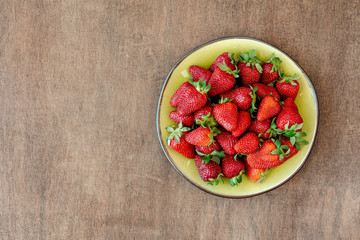 Strawberry in green plate on wooden background. Top view, copy space	