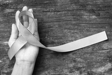 Silver color ribbon on hand support and aged wood (isolated with clipping path) for Parkinson's disease awareness and Brain cancer tumor illness