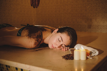 lateral view of a beautiful woman in spa salon having spa therapy with coffee done by a masseur