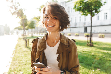 Young pretty woman walking outdoors in park in beautiful spring day using mobile phone.