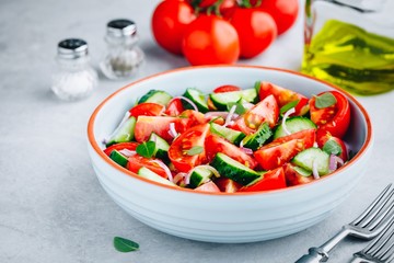 Fresh summer salad bowl with tomatoes, cucumbers, red onions, basil and olive oil dressing.