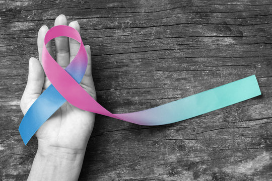 Thyroid Cancer Awareness ribbon Teal Pink Blue ribbon color on woman's helping hand support on old aged wood background (isolated with clipping path)