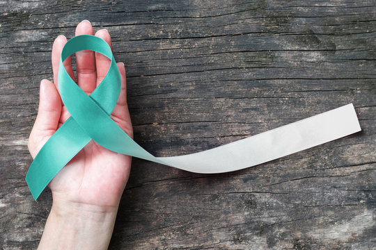 Teal and white ribbon for Cervical Cancer awareness campaign concept symbolic bow color on woman helping hand support on old aged wood