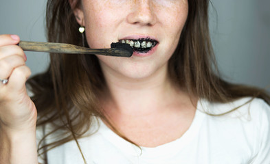 young woman brushing her teeth with a black tooth paste with active charcoal, and black tooth brush on white background for Teeth whitening