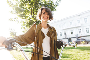 Cute young amazing woman walking outdoors in park with bicycle beautiful spring day.