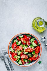 Fresh summer salad bowl with tomatoes, cucumbers, red onions, basil and olive oil dressing.