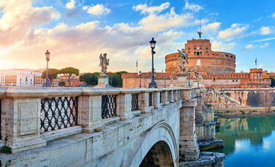 Rome, Italy. Bridge with angels and demons statue in front of Castle of the Holy Angel (Castel Sant Angelo) during evening sunset. Famous touristic landmark. Statues and street lamps medieval.
