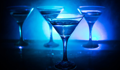 Martini cocktail glass in hand splashing on dark toned smoky background or colorful cocktail in glass with splashes and olives. Party club entertainment. Mixed light. Selective focus
